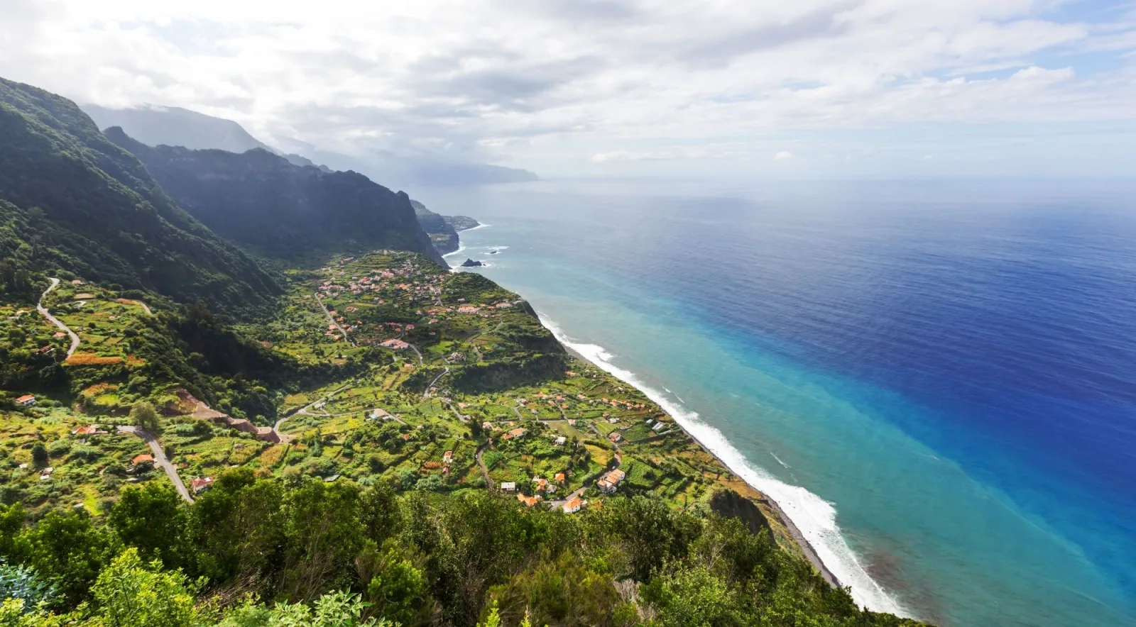 Madeira's north coast from above, terraced village and turquoise shallows meeting deep blue ocean