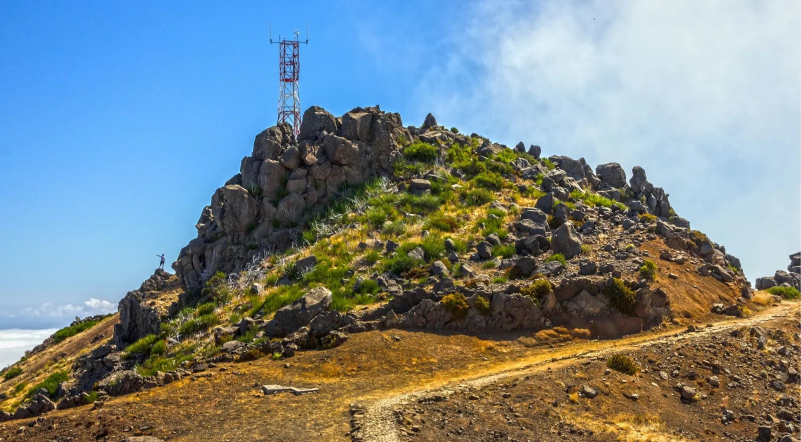 The summit of Pico do Areeiro with its radar tower, a lone walker standing on the rocks below