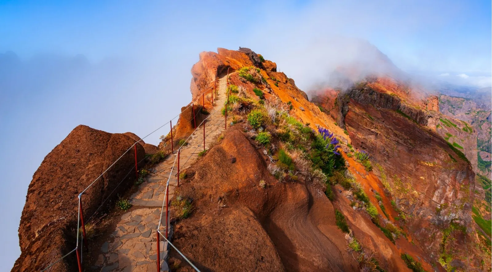 The cable-railed stone path curving along an orange volcanic ridge high above the cloud layer